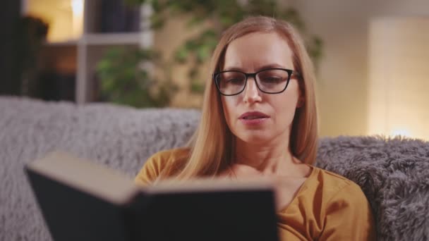 Mujer leyendo libro en sofá — Vídeo de stock