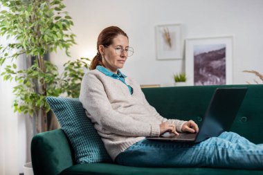 Kanepede dizüstü bilgisayar kullanan kadın.