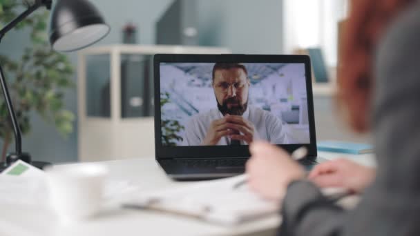 从坐在办公室的高加索女人的肩膀上看 看到笔记本电脑屏幕上有胡子的男同事在领导在线会议 视频聊天 人与合作概念 — 图库视频影像