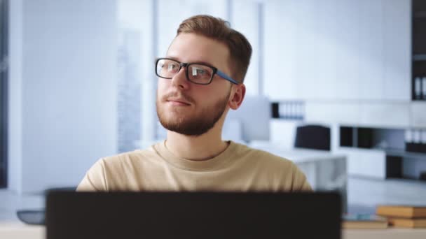 若い男性労働者のノートパソコンでテーブルに座って離れて見て考えている 現代のオフィスでの仕事中に問題解決を検討しています — ストック動画