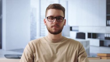 Gündelik giysiler ve gözlüklerle gülümseyen sakallı adamın portresi modern ofiste kollarını kavuşturarak oturuyor. İnsan kavramı, meslek ve başarılı kariyer.