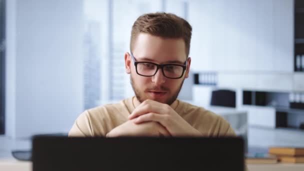 戴眼镜的英俊年轻人坐在写字台前 在视频会议期间聊天 白种人男性员工使用无线笔记本电脑与同事进行在线交流 — 图库视频影像