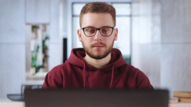 Beyaz tenli, göz giysisi ve günlük kapüşonlu yakışıklı iş günü boyunca laptopun ekranına güvenle bakıyor. Modern bilgisayarda yeni proje geliştiren yaratıcı genç adam.