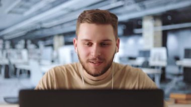 Kafkasyalı, günlük giysiler içinde çalışma alanında oturan ve modern laptopta görüntülü sohbet yapan genç bir adam. İnsan kavramı, iş ve çevrimiçi sohbet.