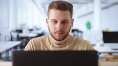 Boş ofis odasında kablosuz bilgisayarda yazan sakallı genç adam. Modern kulaklıklar üzerine odaklanmış girişimci yeni bir proje üzerinde çalışıyor. İnsanlar ve teknoloji kavramı.