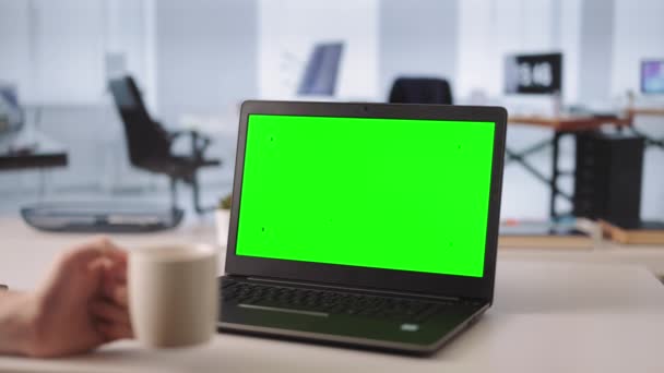 办公室工作人员在现代笔记本电脑上工作的特写镜头 手里拿着一杯清晨咖啡 专注于有绿色空屏幕的手提电脑 — 图库视频影像