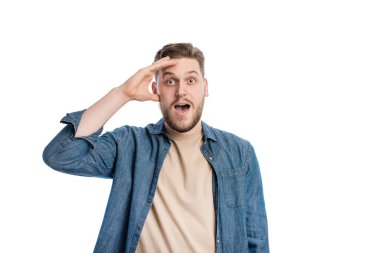 Heyecanlı genç bir erkek, eli yüzü üzerinde, şaşkın bir şekilde dik dik bakıyor. Beyaz stüdyoda ağzı ve gözleri açık duygusal bir adamın portresi..