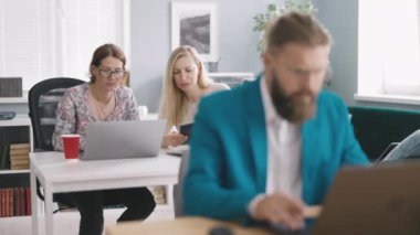 Ofiste tartışırken modern dizüstü bilgisayar ve dijital tablet kullanan iki bayan meslektaşım. İş yerinde oturan Kafkas işadamının bulanık önplanı.