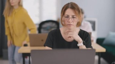 Günlük giysiler içinde iki beyaz kadın işyerinde ortak bir projeyi tartışıyorlar. Bilgisayarlı ofis çalışanları şirkette başarılı olmak için işbirliği yapıyorlar..