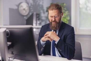 Caucasian businessman in formal wear with wry grimace sitting at workplace and looking on pc monitor. Facial expression, technology and people concert.