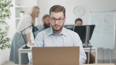 Young office worker surprised using laptop. Excited colleagues happy for him, teamwork concept.
