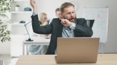 Mature bearded man having fun in office workplace, dancing near laptop, carefree lifestyle concept