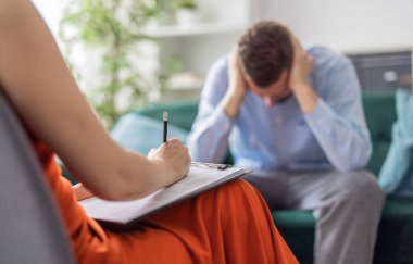 Psychologist doctor woman making notes during a therapy session with patient, mental health care concept