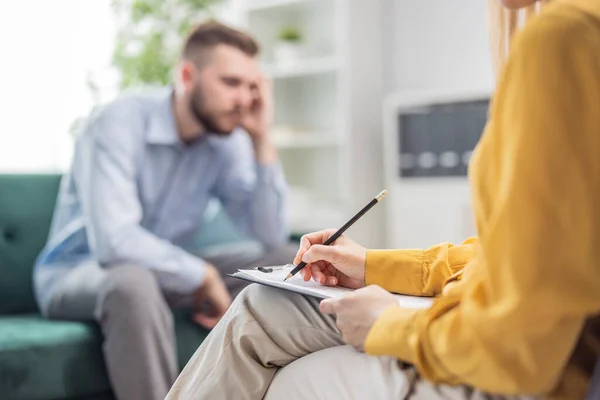 Psychologist doctor woman making notes during a therapy session with man client, mental health care concept