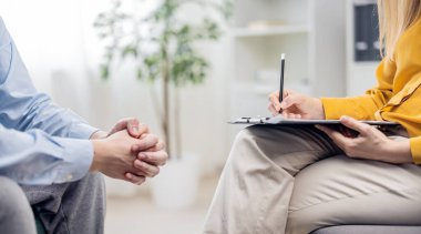 Middle view of psychologist woman doctor making notes consulting male patient in bright office