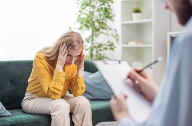 Depressed woman talking about her problems, session of psychology and mental health support, doctor meking notes in bright office