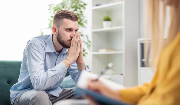 Depressed man talking about problem, psychologist session in bright office, mental healthcare concept