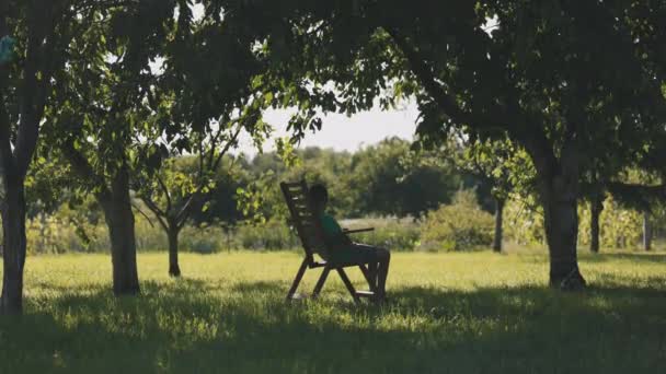 快適な椅子に座って庭でリラックスした少年 夏の家で屋外の子供時代 — ストック動画