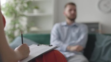 Kadın tıp doktoru psikolog, erkek hasta ve akıl sağlığı konseptini dinlerken not alıyor.