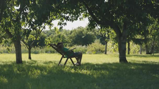 Chlapec Chladící Zahradě Sedí Pohodlném Křesle Pod Stromy Dvorku — Stock video