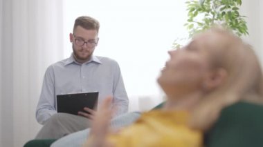 Stresli sarışın kadın zihinsel sorunlardan bahsediyor, genç doktor psikolog not alıyor, profesyonel sağlık konsepti