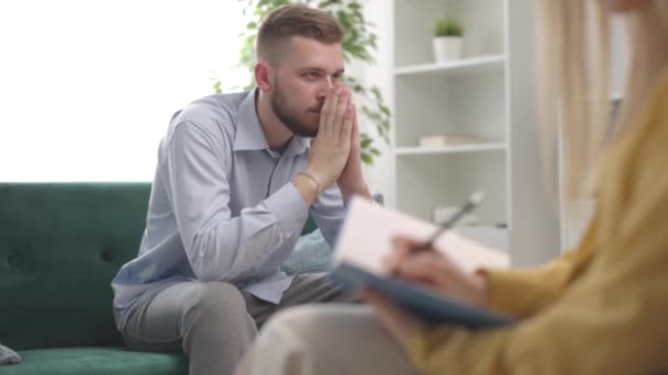 Głęboko Myślący Zestresowany Mężczyzna Podczas Sesji Psychologicznej Terapeutka Robiąca Notatki — Wideo stockowe