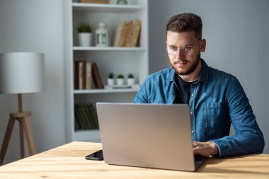 Kot gömlekli sakallı adam evde dizüstü bilgisayarda çalışıyor.