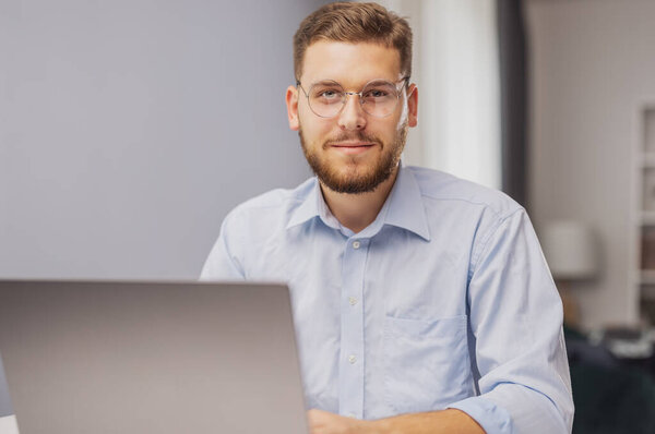 Portrait of young bearded businessman sitting at desk with laptop