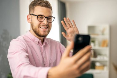 Genç yakışıklı adam akıllı telefondan video bağlantısı kuruyor, uzaktan konuşuyor.