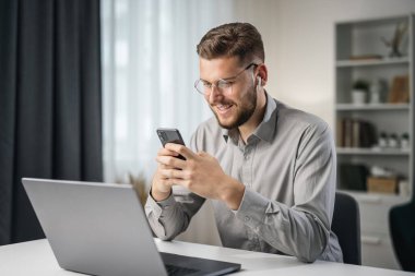 Mutlu gülümseyen yakışıklı adam mesajlaşmak için akıllı telefonu kullan, evde öğrenci uygulaması kullan