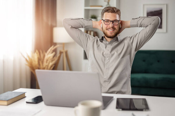 Happy businessman at laptop desk with gadgets, handsome male working remotely from home, success concept