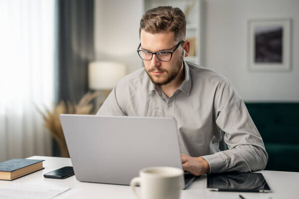 Young handsome man coding with at laptop from home, remote work, intelligent coder writing software code