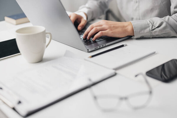 Top view of business white desk, cropped businessman typing on laptop next to paper documents and cup, office workplace