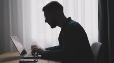 Laptopta yazan yakışıklı sakallı adam, kod yazan genç adam, pencere ışıklarına yaslan