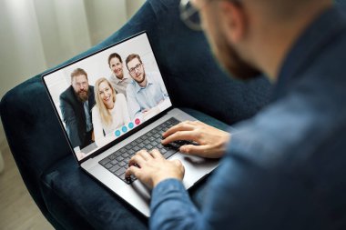 Kot ceketli genç adam, internete bağlanan genç iş adamlarından oluşan dizüstü bilgisayardaki görüntülü sohbeti kullanarak sohbet ediyor.