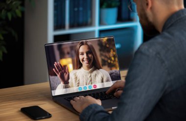 Evde sevgilisiyle görüntülü görüşme yapan bir adam, dizüstü bilgisayarında el sallayan genç ve neşeli bir bayan.