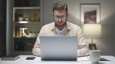 Akşamları geç saatlerde evde dizüstü bilgisayarı ve akıllı telefonuyla çalışan beyaz bir iş adamı.
