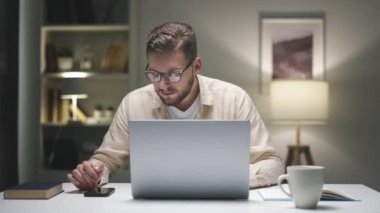 Geceleri evde dizüstü bilgisayar başında çalışan, akıllı telefonları kaydıran ve faturaları internetten ödeyen bir adam.