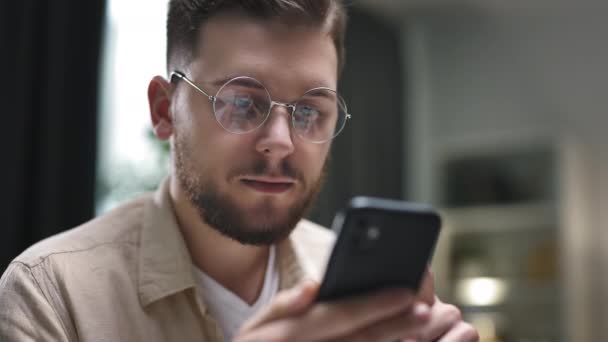 身着圆形眼镜的年轻高加索男性 一边滚动智能手机 一边检查社交媒体和电子邮件 — 图库视频影像
