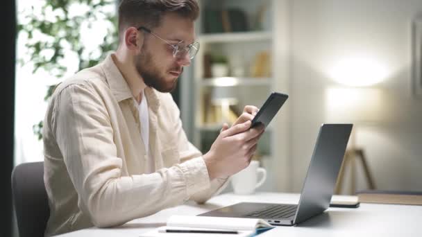 Jovem Caucasiano Masculino Rolagem Smartphone Verificação Informações Sobre Laptop Fornecendo — Vídeo de Stock