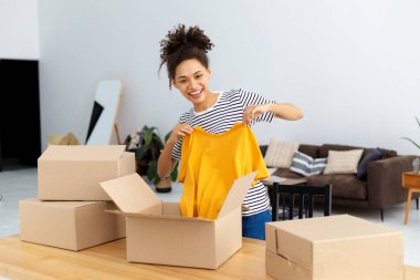 Afrikalı Amerikalı kadın blogcu vlogger serbest yazar takipçileri için canlı yayın yapmak için webcam kullanıyor. Sipariş edilmiş kıyafetleri, ürünleri gözden geçiriyor. Kamerada paketleri açan genç bir kadın gülümsüyor.