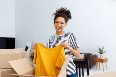 Afrikalı Amerikalı kadın blogcu vlogger serbest yazar takipçileri için canlı yayın yapmak için webcam kullanıyor. Sipariş edilmiş kıyafetleri, ürünleri gözden geçiriyor. Kamerada paketleri açan genç bir kadın gülümsüyor.