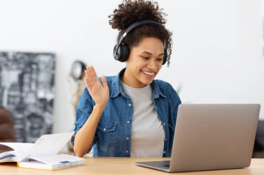 Kulaklıklı mutlu Afrikalı Amerikalı kız öğrencinin portresi dizüstü bilgisayarla modern ofiste ya da evde otururken görüntülü konuşma yaparak dil öğreniyor. Freelancer uzaktan çalışıyor, bir şeyi tartışıyor.