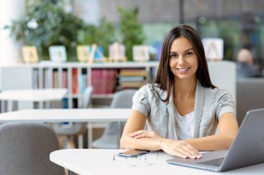 Öğrenme, online eğitim. İş yerinde çalışan serbest çalışan kadın ya da çalışan birinin portresi. Gülümseyen beyaz kadın dizüstü bilgisayar kullanıyor, modern ofiste çalışıyor, arkadaşça gülümsüyor.