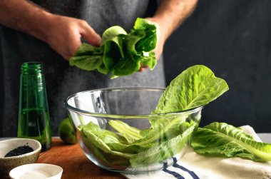 Adam romaine yapraklarından sağlıklı yeşil salata pişiriyor. Sağlıklı gıda konsepti