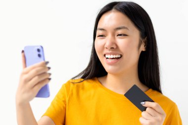 İnternetten alışveriş, teknoloji konsepti. Beyaz arka planda cep telefonu ve kredi kartı tutan mutlu Asyalı kadın.