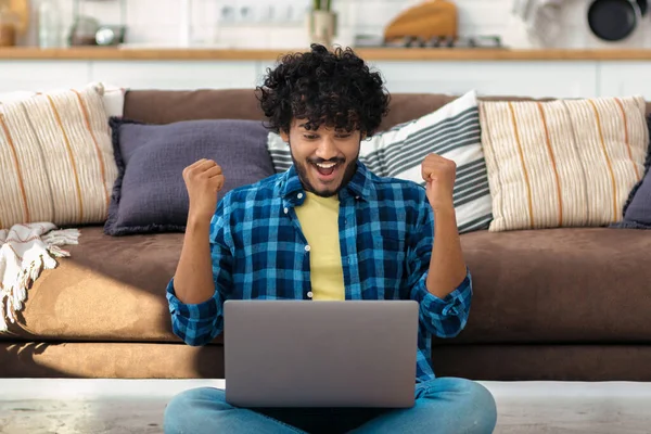 Portrait of excited young Asian man celebrating success while sitting with laptop at home. Happy male freelancer working, he receive good news by email