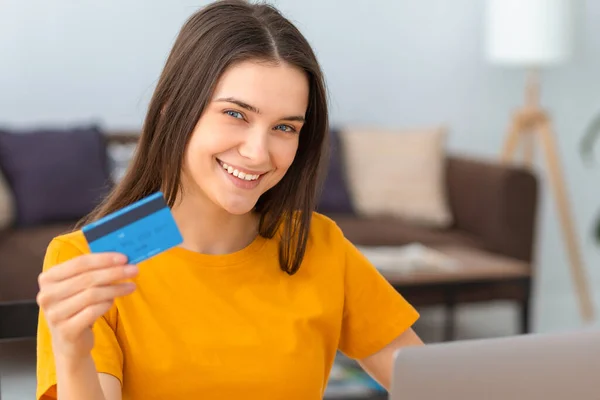 Young caucasian woman hold bank credit card, shopping online using laptop computer, buying goods or ordering online. Female holding a bank credit card in his hands and smiles friendly at the camera