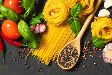 Spaghetti and tagliatelle with tomatoes, pepper, garlic and parsley on dark background, top view. Italian food cuisine and ingredients concept