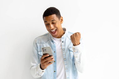 Young joyful man using mobile phone and smiles. Male holding smartphone in his hands looking at the screen, reads a message good news, plays games, victory, success